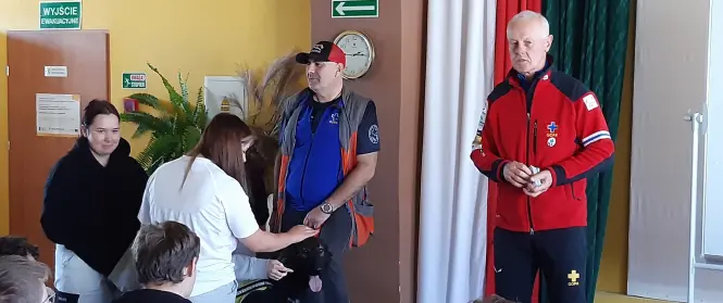 Na zdjęciu dwóch goprowców z psem na wykładzie w sali lekcyjnej